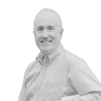 Black-and-white portrait of a smiling older white man with short, light-colored hair, wearing a light-colored button-down shirt and facing the camera against a plain white background.