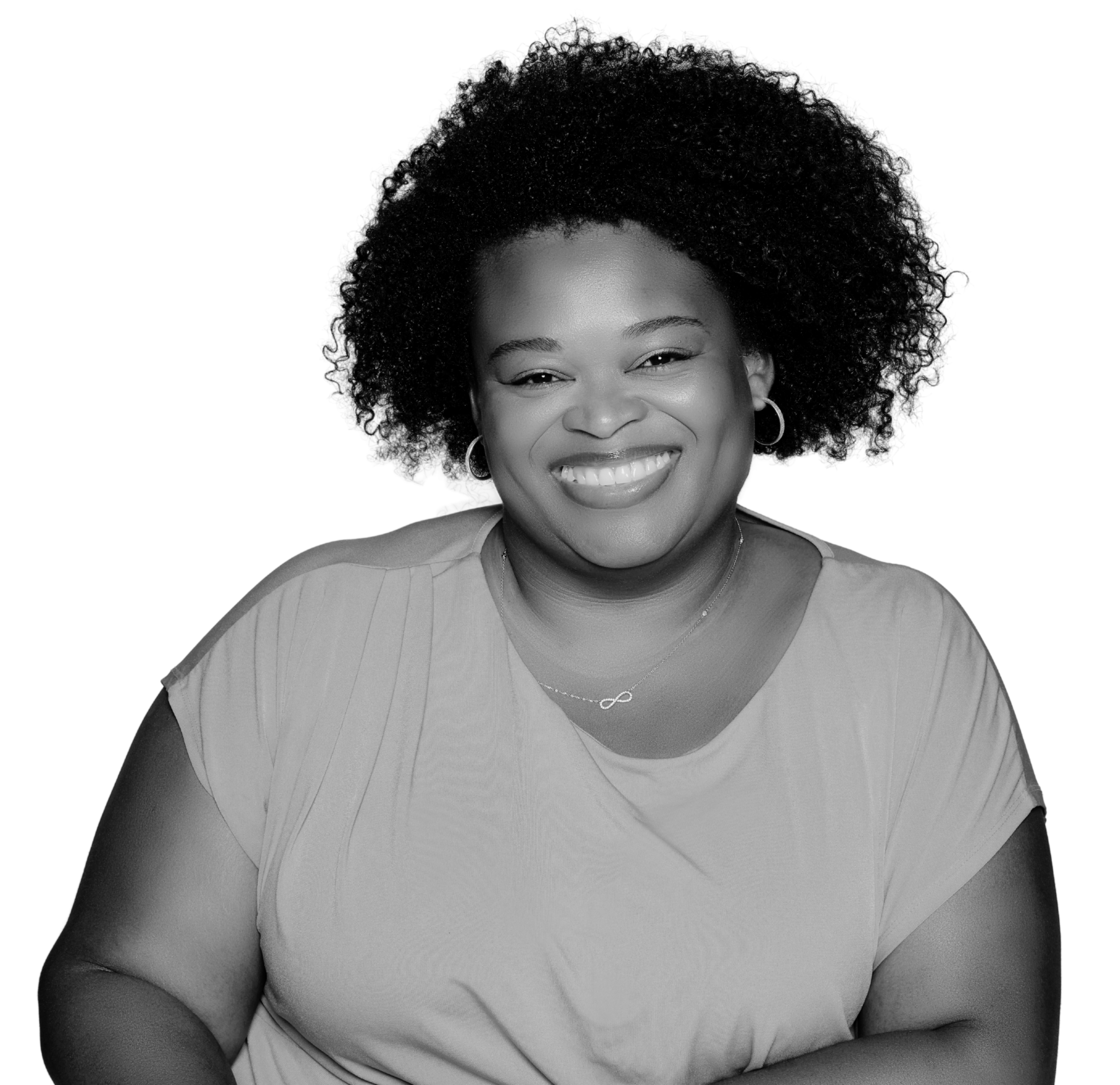 Black-and-white portrait of a smiling woman with natural curly afro hair, wearing hoop earrings, a light-colored top, and a delicate infinity necklace against a plain background.